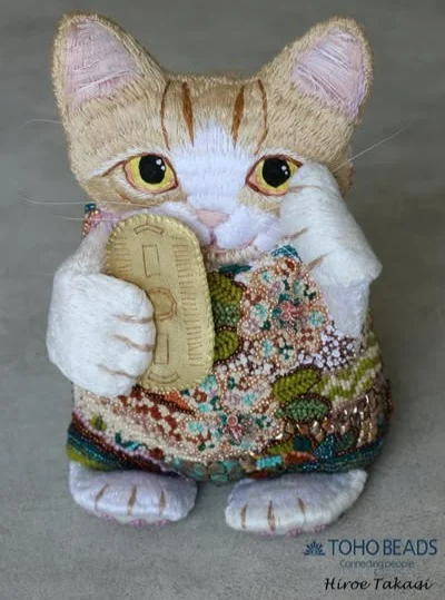 TOHO Challenge 2025 “Sonoran Sunset”
Featured Designer: Hiroe Takagi （髙木　洋恵）~TOHO BEADS Advanced Designer~
@hiroe_takagi_beads_fan_ 
http://www.beads-fan.jp
Title: Maneki-neko招き猫～Mocha(モカ）～

「招き猫は、日本の伝統文化に深く根ざした縁起物です。左手を挙げた招き猫は”人を招く”という意味があります。マンチカンのモカは、手足が短いので、一生懸命手を挙げています(笑）今年のイメージカラーのソノラ砂漠の夕日と、モカの優しいベージュカラーの毛並みとの融合と、ボディは、砂漠のサボテンと、日本の和柄の市松模様、桜モチーフを合わせて流れるようにつなげ、接ぎ目をなくし、立体的に仕上げました。ヒゲは、モカの本当のヒゲを使っています。」

“The Maneki-neko (beckoning cat) is a talisman deeply rooted in Japanese traditional culture. The name literally means a cat (neko) with its left paw raised beckoning (maneki) to passersby. Mocha, a Munchkin with naturally short legs, is really trying her best to raise her paw (lol).
The piece depicts this year’s color image of the Sonoran Sunset blending with Mocha’s soft beige coat and a flowing, seamless combination of cacti with a Japanese checkered pattern and cherry blossoms on the body, all worked up three-dimensionally. Those are Mocha’s real-life whiskers. “

モカから一言：「Hi, everyone! 全方位見てニャ！足の肉球もビーズになっているんだニャ～。ヒゲは、モカの本当のヒゲだニャン！」

Mocha's comments: "Hi, everyone! Get a good look from all sides! Even my paw pads are beads! Miaow! These are Mocha’s very own whiskers, too!"

#tohobeads #tohochallenge2025 #teamtohobeads #starmanbeads #bobbybeadstore #twinklebeadsdortmund #ilovetohobeads #tohobeadsconnectingpeople #glassbeadart #tohochallenge